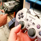 A hand holds up a PlayStation 1 controller in front of a demo kiosk.